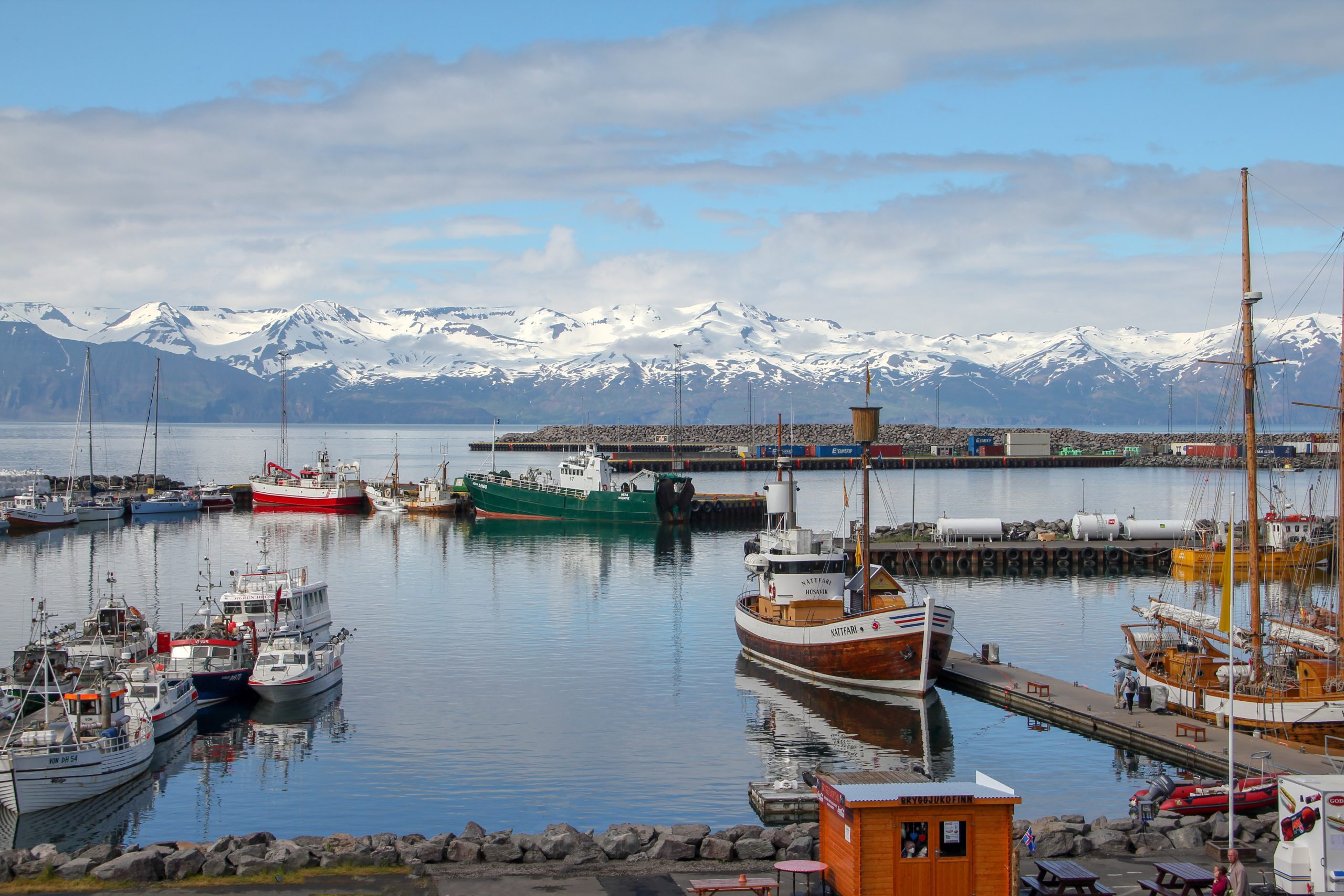 Boats moored in a harbour with snow covered mountains in the background